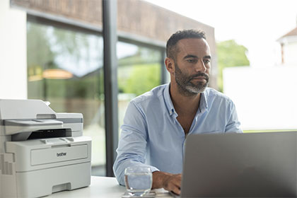 Male sat at desk using laptop, Brother MFC-L2922DW on desk