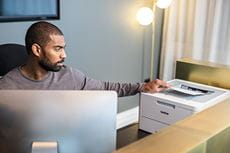 Mężczyzna siedzi przy biurku na recepcji, drukarka Brother HL-L8230CDW, monitor