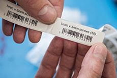 Ръце държат отпечатани етикети, показващи информация за продукт и баркодове