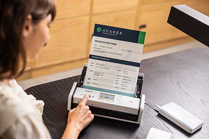 Osoba siedząca przy biurku naciska klawisz skanera Brother ADS-1800W zasilanego przez powerbank