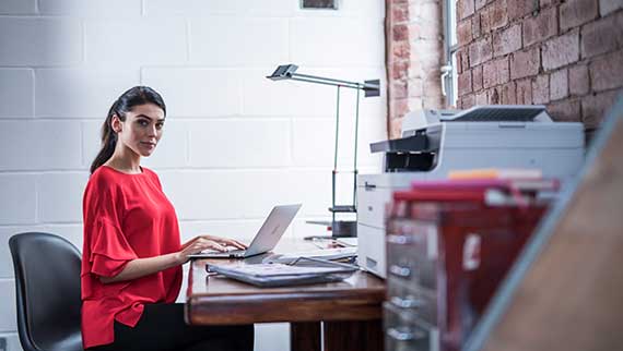 žena v červenom tope sediaca za stolom, pracujúca s laptopom, tlačiareň Brother