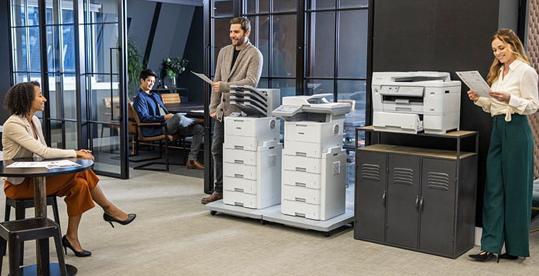 Birou mare și aglomerat, cu un rând de imprimante Brother. Doi bărbați, două femei, dulap, birouri, scaune