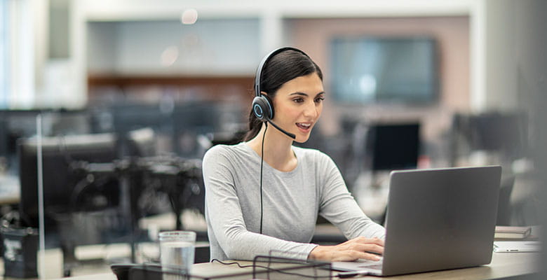 Жена, носеща слушалки, работи на лаптоп в голям офис