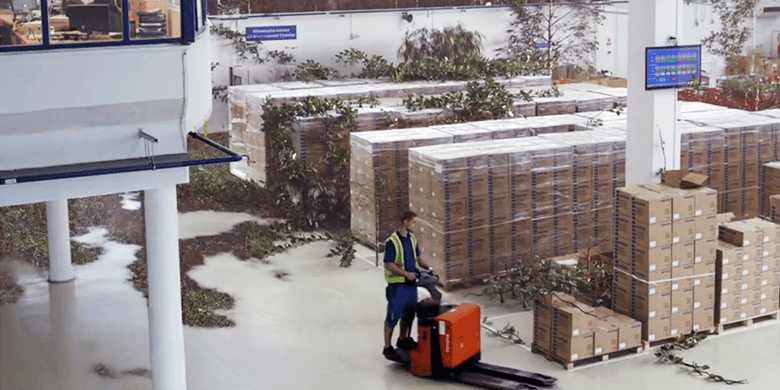 muž s vysokozdvižným vozíkom vo výrobnej hale obklopený krabicami a stromami