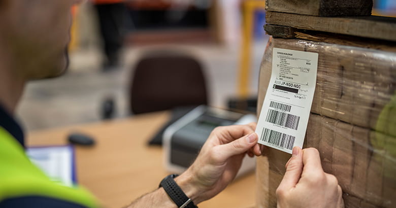 Pracovník v továrně umísťuje štítek na balíček pomocí přímého termálního tisku