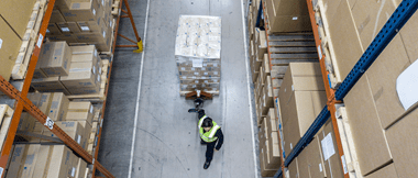 Un employé d'entrepôt tire un chariot d'appareils Brother emballés et étiquetés dans un entrepôt, prêts à être transportés.