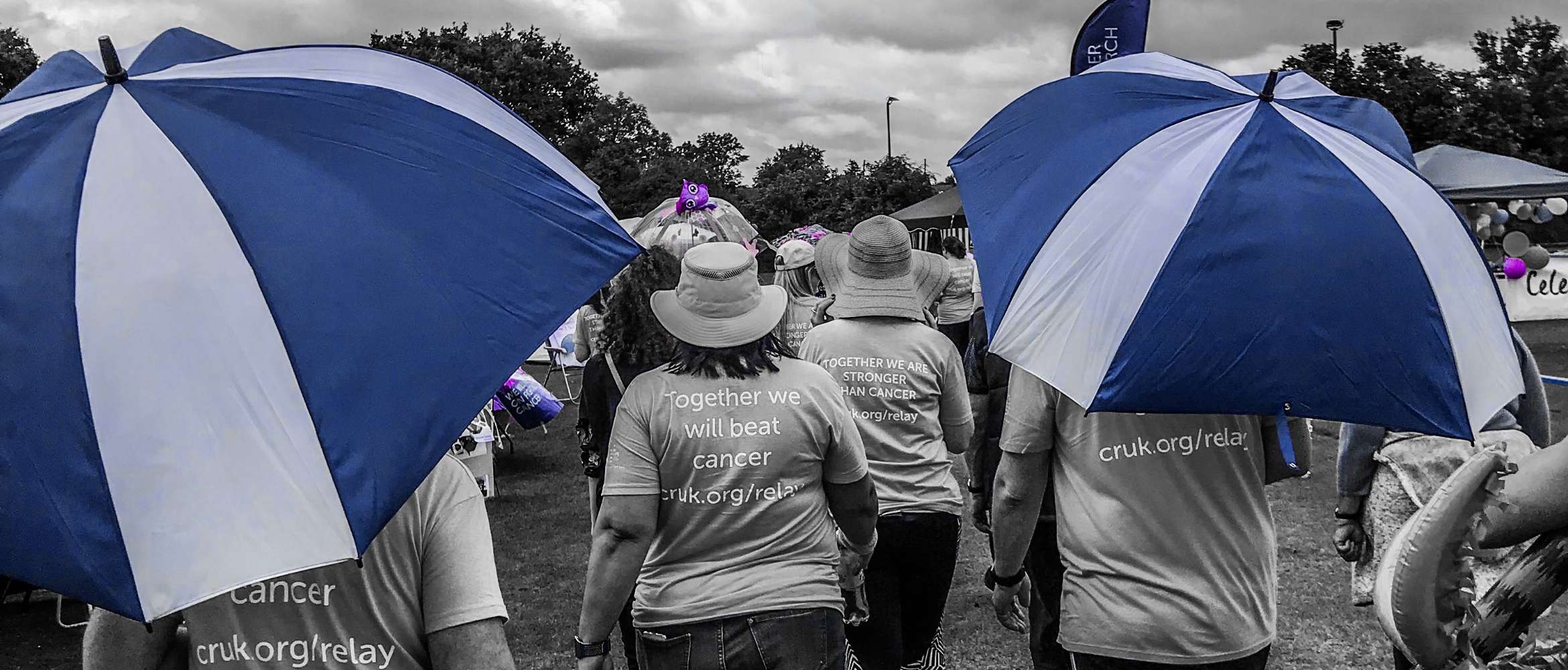 Schwarzweissfoto mit blauen und violetten Farbtupfern zur Illustration des Wohltätigkeitslaufs Relay for Life mit Dutzenden von Menschen, die beim Sammeln von Spenden für wohltätige Zwecke helfen.