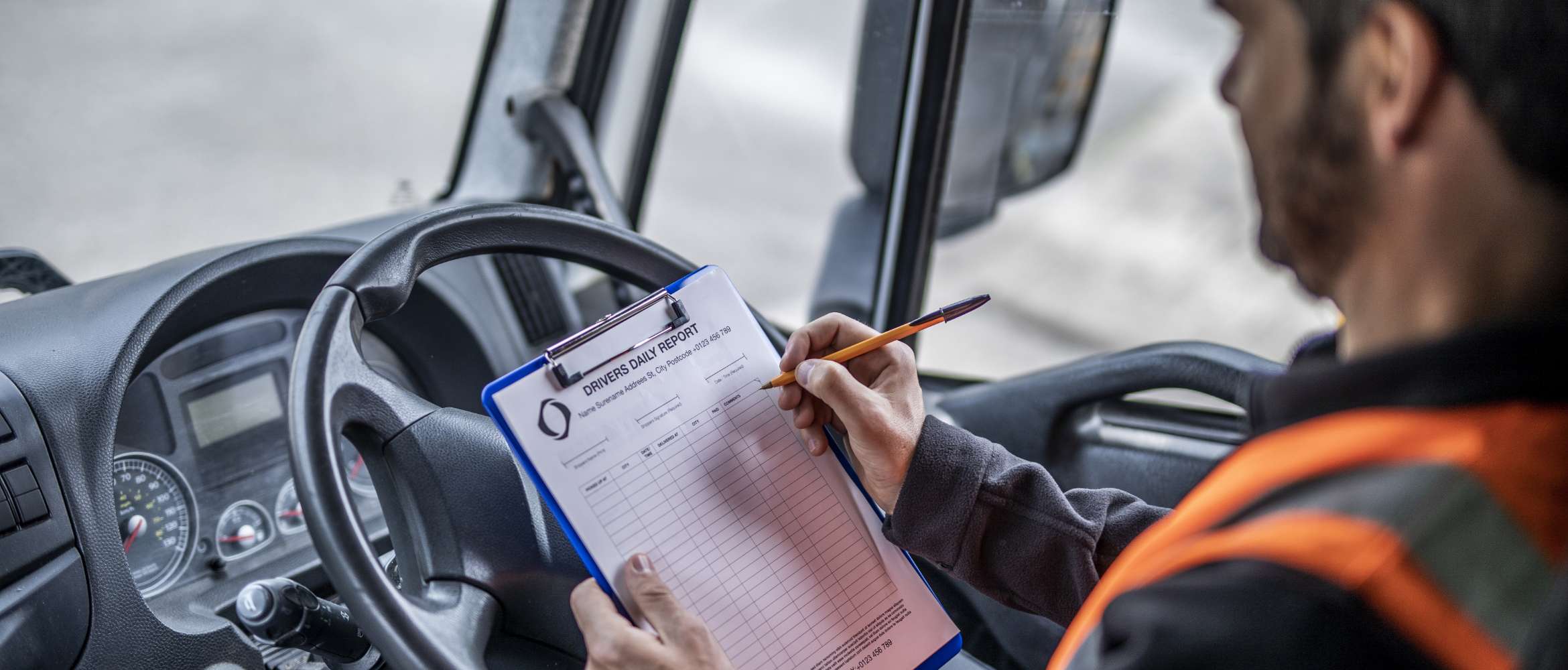 Ein Kurier aus der Transport- und Logistikbranche überprüft in der Führerkabine seines Lieferwagens eine ausgedruckte Checkliste.