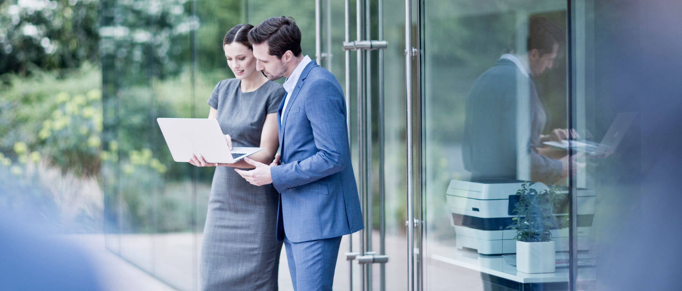 Man and woman typing on a laptop and talking outside office