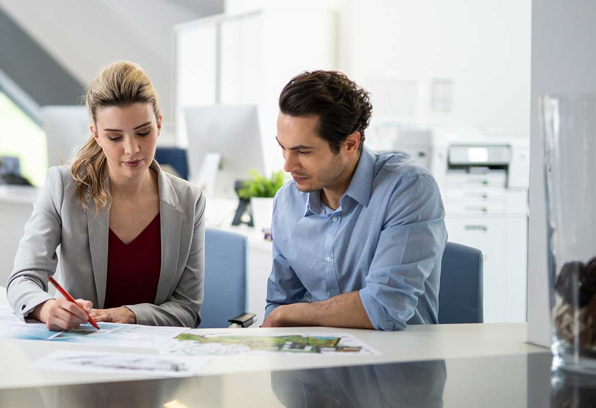 Male in shirt and female in smart clothing sat looking at document which the female is working on with the pen in her hand