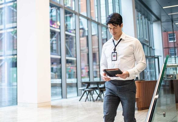 Male in shirt wearing office badge and carrying a book walking through an enterprise environment with glass walls
