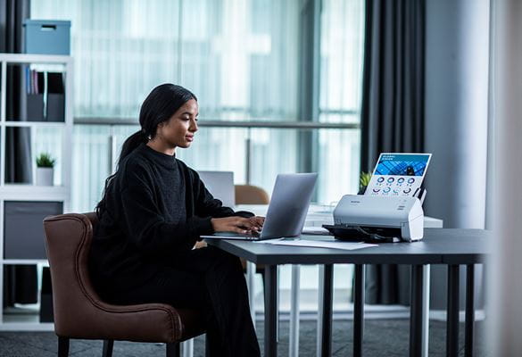 Frau sitzt an einem Laptop und ist dabei ein Dokument zu scannen