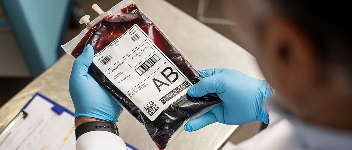 Labormitarbeiter hält einen Blutbeutel mit Etikett in der Hand. 