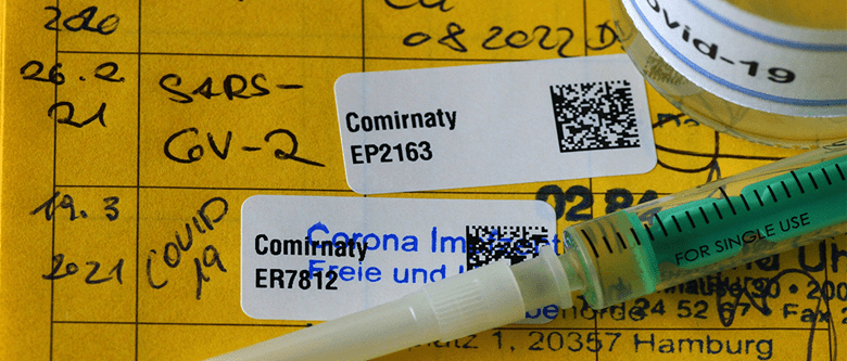 Impfpass mit Etikett von Coronaschutzimpfung, Spritze und Ampulle.