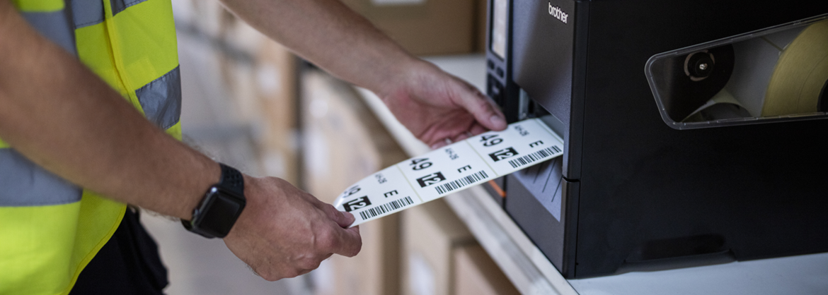 Ein Mensch zieht Etiketten aus einem Etikettendrucker.