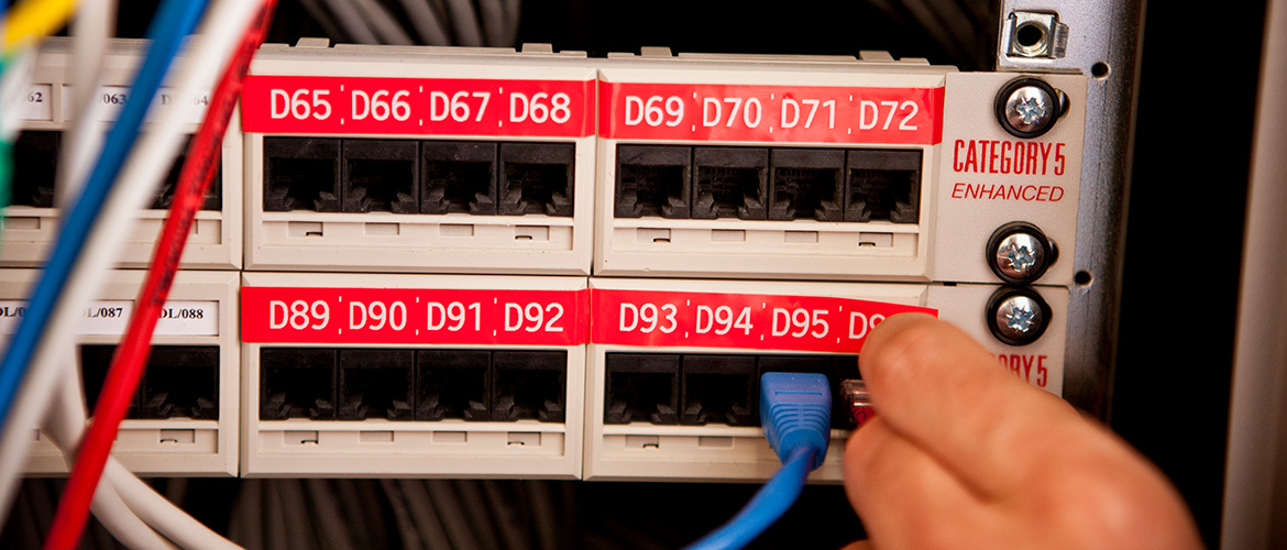 Hand steckt einen Netzwerkstecker in einen Schaltschrank.