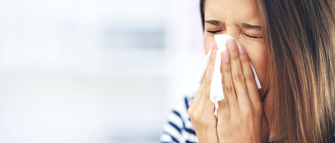 Das Bild zeigt eine Frau, die sich aufgrund ihrer Allergie die Nase putzt.