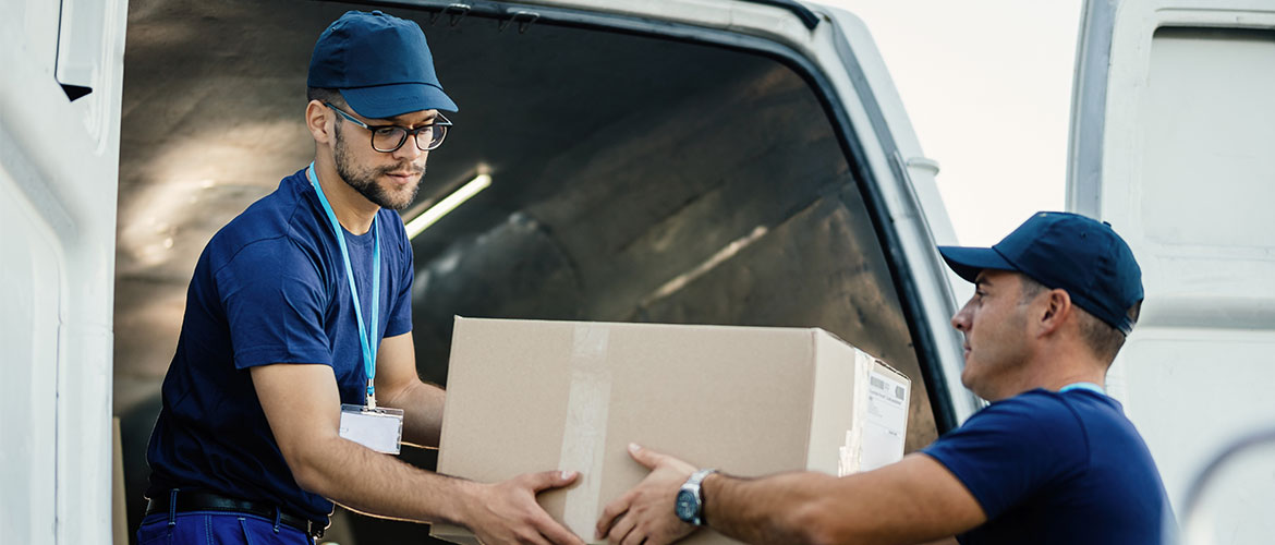Zwei Männer, die gemeinsam aus einem Lieferwagen ein Paket entladen.