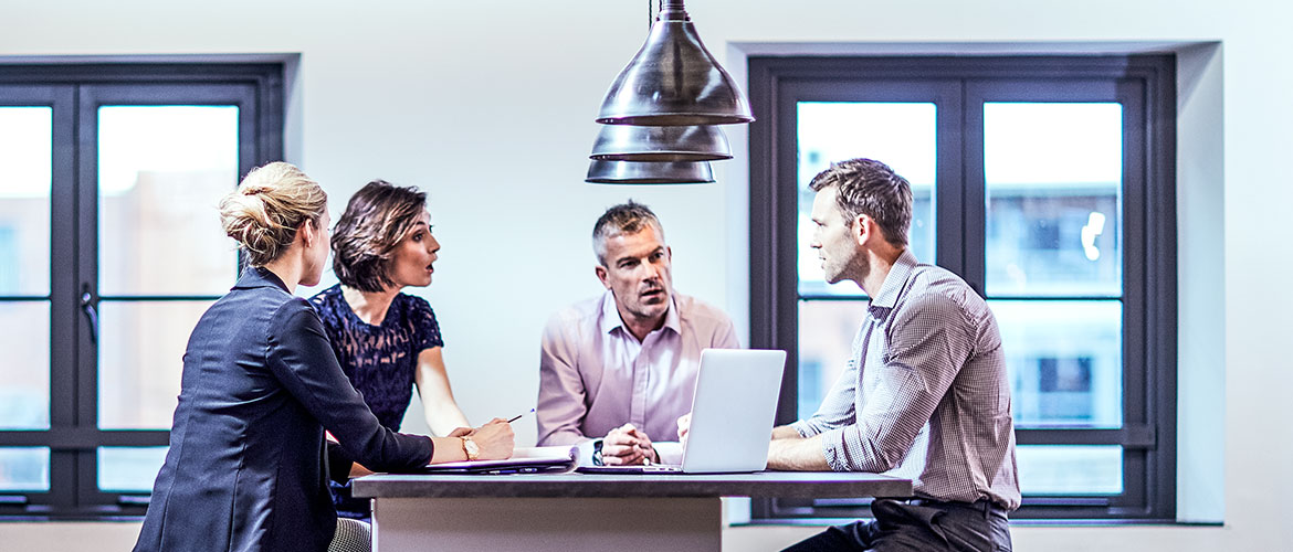 Vier Menschen sitzen ein Bürotisch und diskutieren