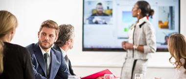 Personen in einem Meetingraum unterhalten sich über Videokonferenz.