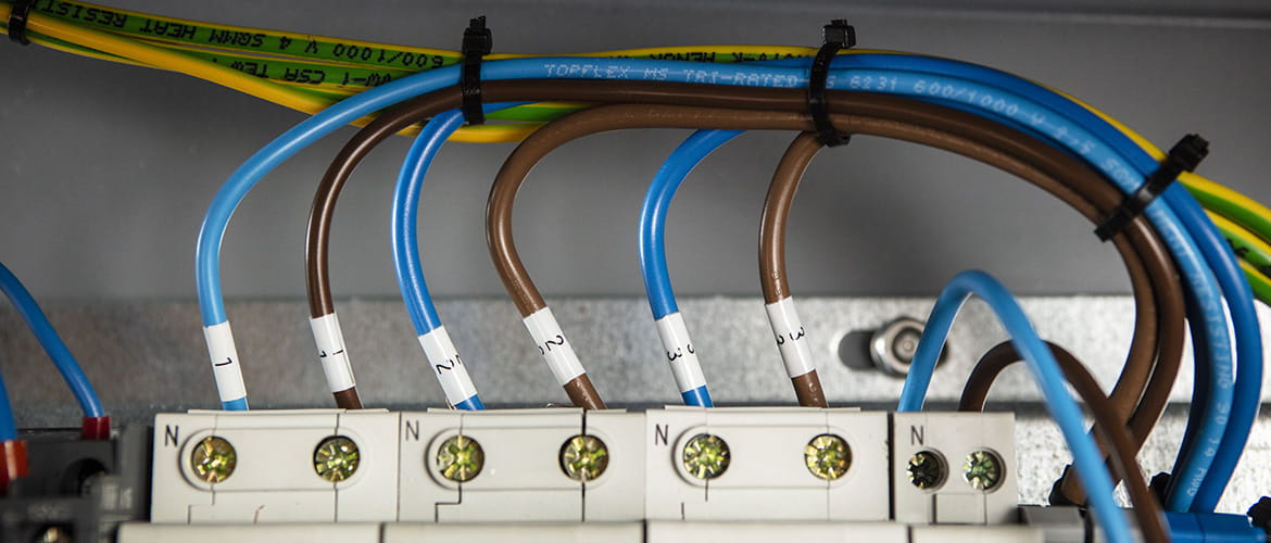 Blaue und braune Kabel in einem Schaltschrank, die per Schrumpfschlauch beschriftet sind. 