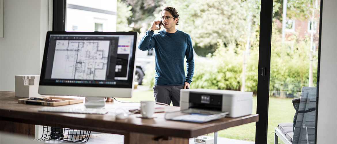 Mann telefoniert im Home Office, Bildschirm und Drucker im Vordergrund