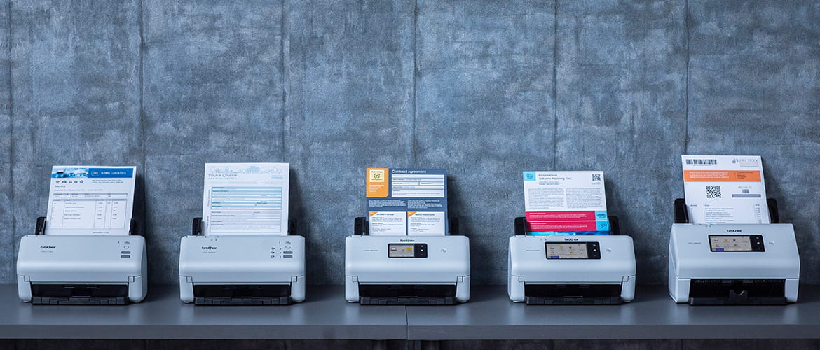 Fünf weiße Dokumentenscanner der Brother ADS4-Serie mit Dokumenten im ADF-Einzug stehen auf einem Tisch nebeneinander.