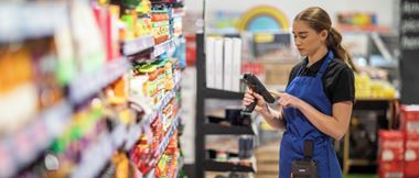 Eine Mitarbeiterin mit einem Scanner in der Hand vor einem Regal, die sich mit den Etiketten im Einzelhandel beschäftigt.