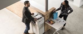 Ein Mann und eine Frau stehen im Büro an einem Brother Drucker und unterhalten sich.