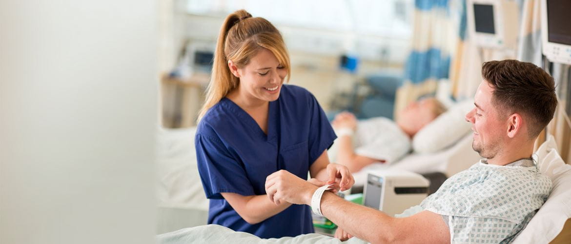 Krankenschwester, lächelnd, legt Patient bedrucktes Patientenarmband an
