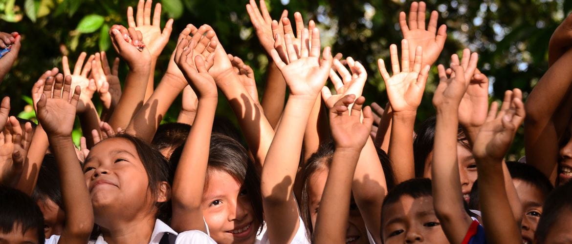 Crowd of smiling children with hands in the air reaching up to the sky