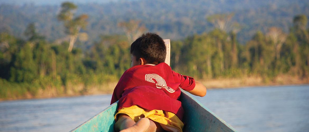 Junge auf einem Fischerboot liegend, welches auf einem Fluss im Regenwald schwimmt