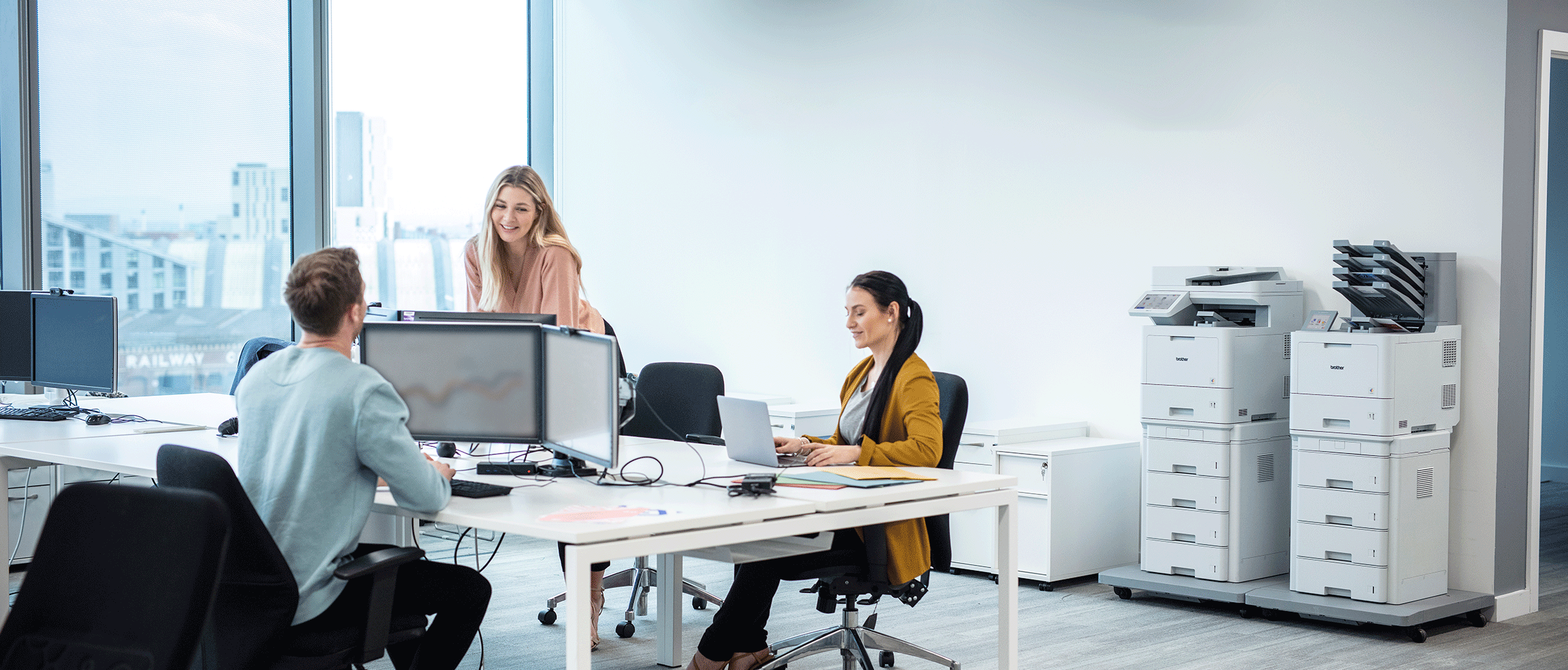 Drei Frauen und ein Mann arbeiten in einem Büro. Brother Drucker im Hintergrund.