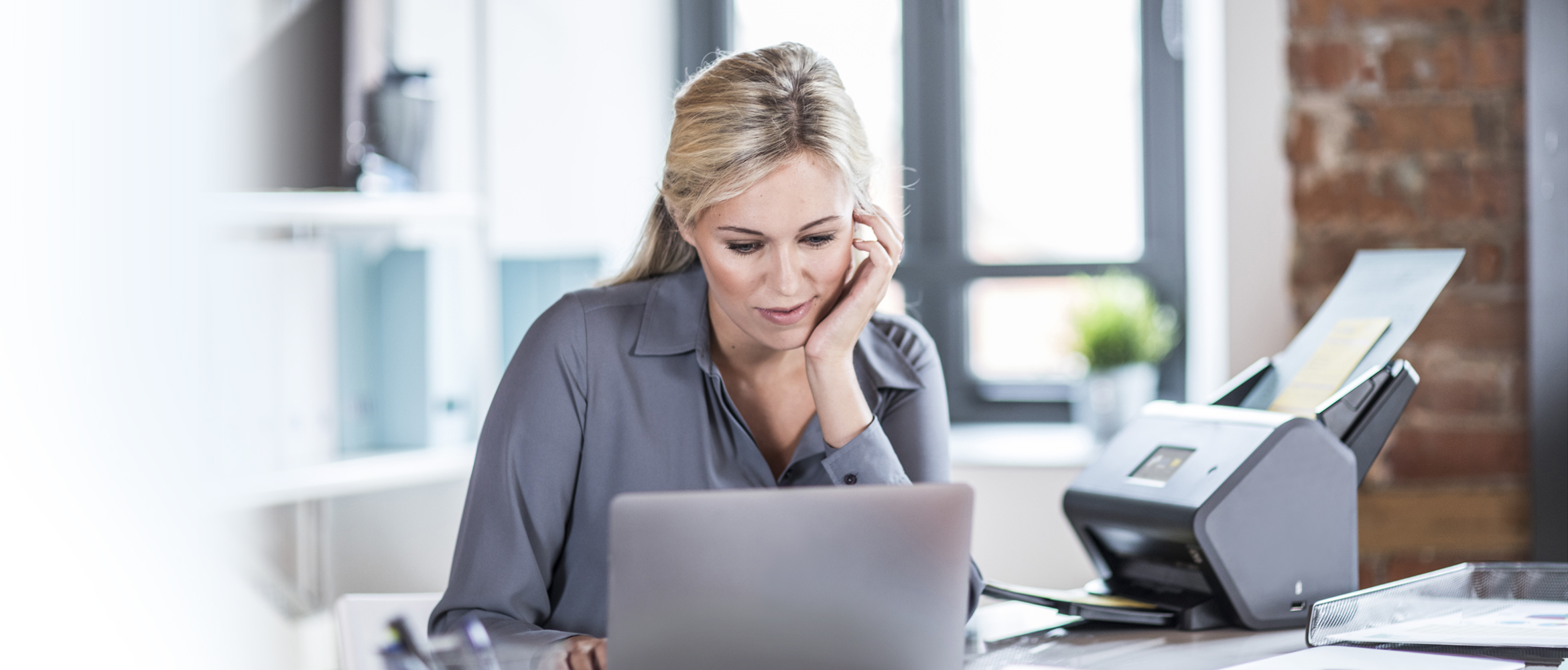 Frau am Schreibtisch sitend, Schaut in Laptop, Brother Scanner Daneben