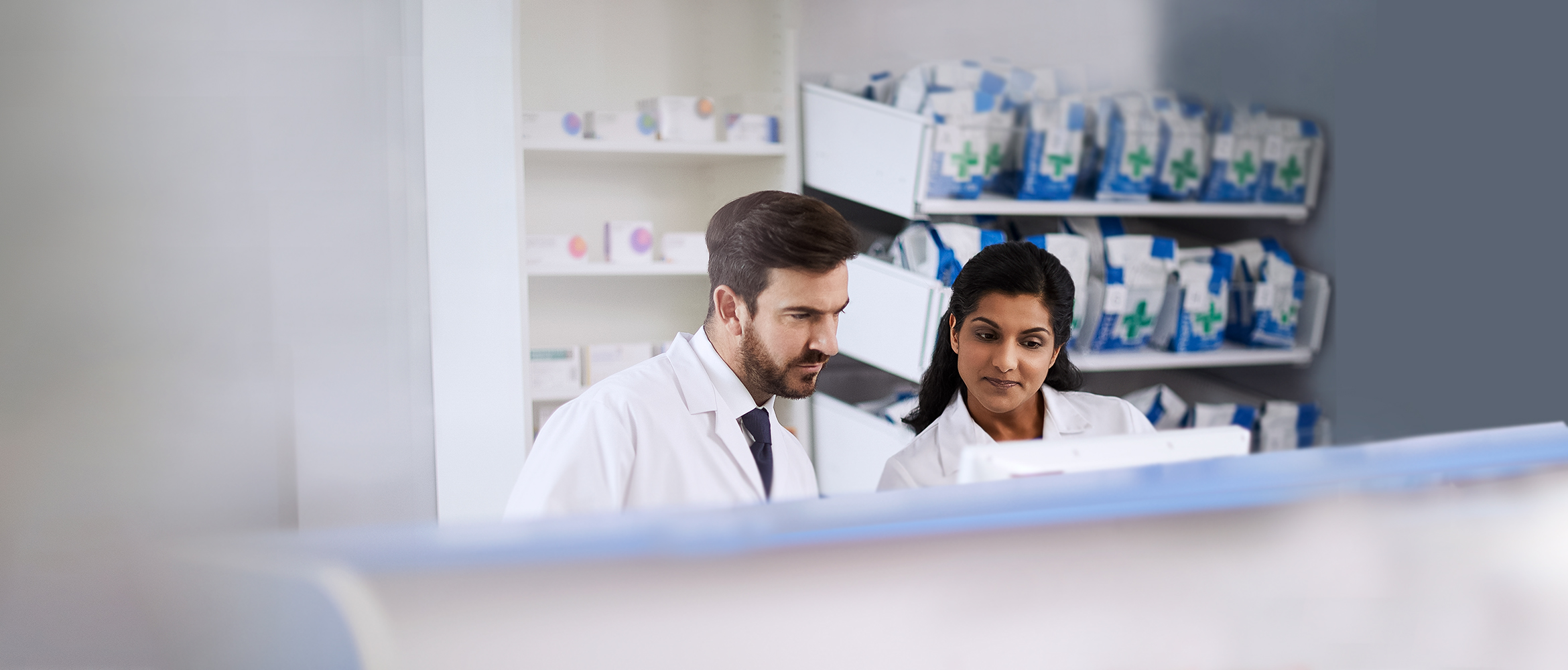 Zwei krankenhausmitarbeiteiter vor Regal mit Medikamente.