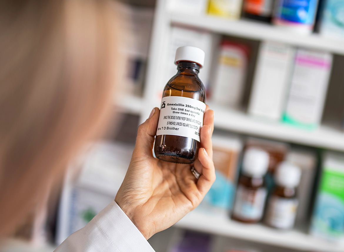 Apotheken-Mitarbeiterin Hält MedikamenteFlasche mit Brother-Etikett, Regal mit Medikamente im Hintergrund