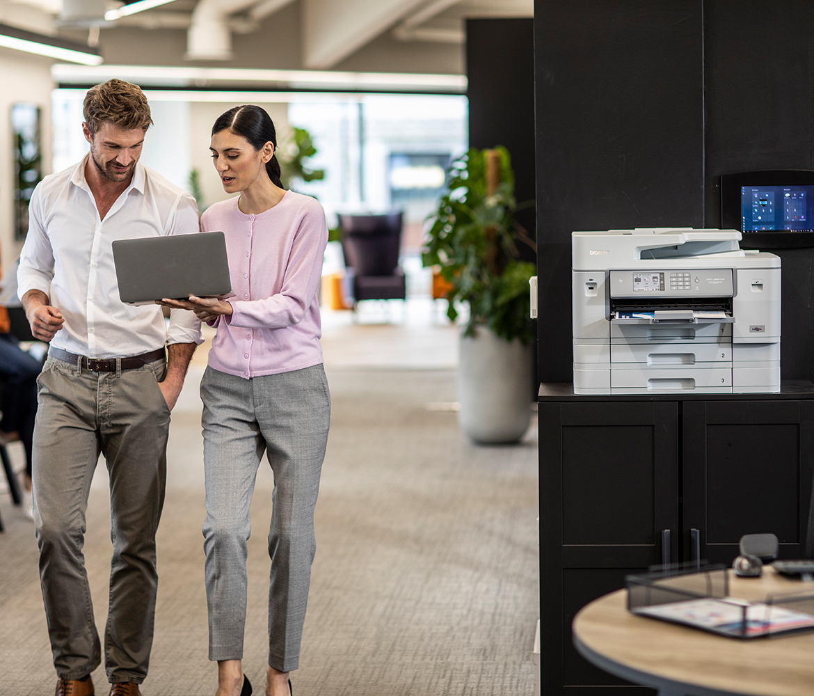 Zwei Personen laufen mit einem Laptop durch ein Büro und unterhalten sich