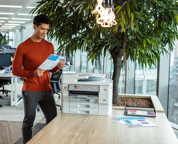 Ein Mann steht im Büro an einem Brother Drucker und liest ein Dokument