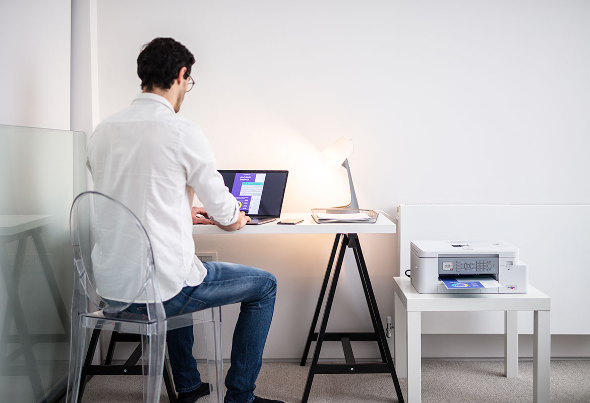 Ein Mann sitzt am Laptop, Brother Drucker neben ihm