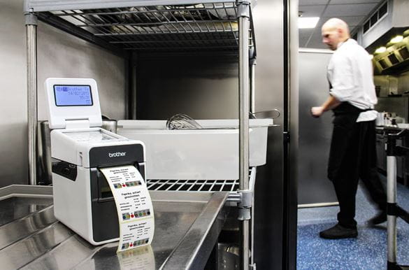 Td-etikettendrucker druckt WareRotationsSetiketten in Restaurant-Küche, Koch im Hintergrunder einer Kühlschrank