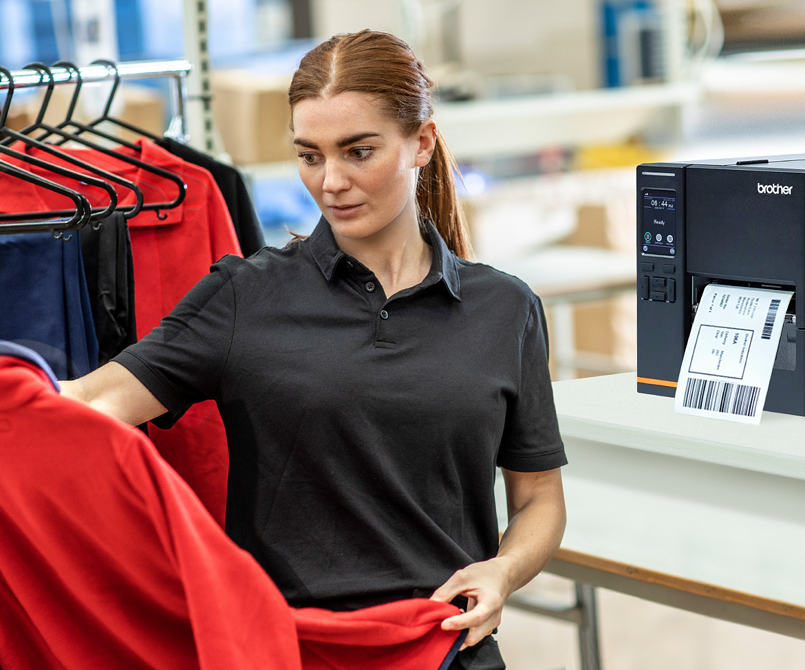 Frau in Sortierentrum Begutachtet ROTE FLEECEJACKE auf Kleiderbügel. TJ-Industrierucker im Hintergrund
