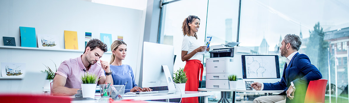 Vier Personen sind in einem Büro am arbeiten. Zwei Personen unterhalten sich. 