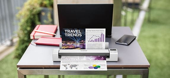 Brother DS-620 Tragbarer Dokumentscanner, der ein Farbdokument auf Tabelle, Laptop, orangefarbenes Notizbuch, Handy, Gras, Im Freien scannt