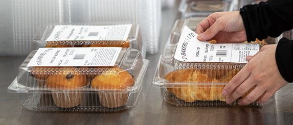 Hände bringt Brother Etiketten auf Plastikverpackung auf, Muffins und Croissants