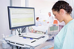 Krankenschwester im Patientenzimmer, an Computer stehend, gibt Daten dein