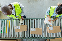 Zwei Personen in Warnwesten überprüfen etikettierte braune Kisten