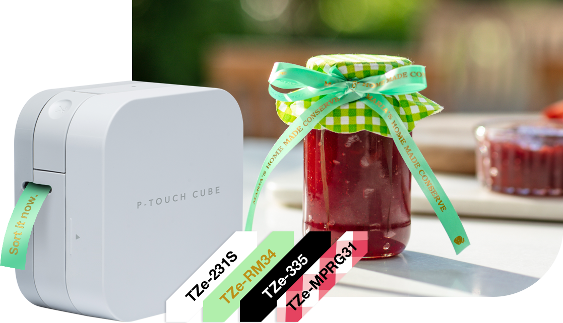 P-Touch Cube mit Grünem Textiletikett, Tzei-Schriffbänder Daneben, Marmeladenglas mit Grünem Textilband im Hintergrund