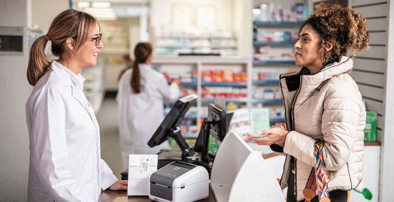 Pharmacist talking to customer over counter with Brother TD desktop printer