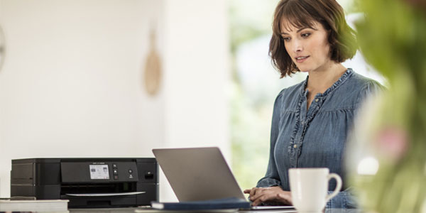 Frau am Laptop mit Drucker im Hintergrund