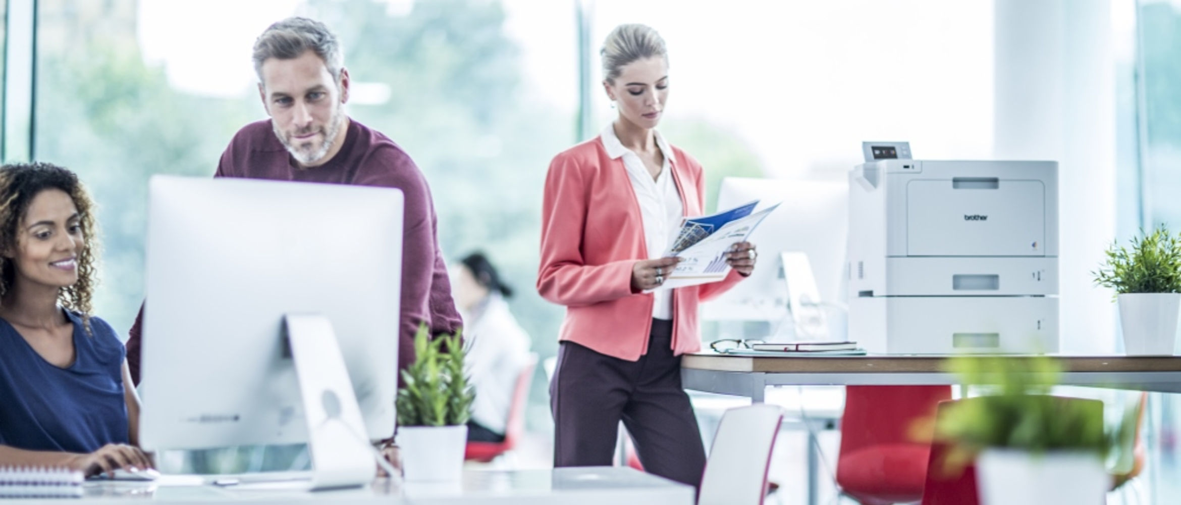 Oficina con tres personas con impresora HL-L9310CDW al fondo.